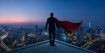 A super hero standing on top of a building with a red cape blowing along side him in the breeze