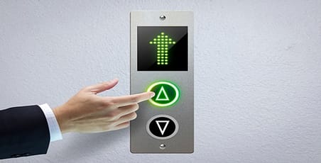 A finger along side an illuminated elevator arrow up button