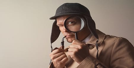 Man dressed as Sherlock Holmes with pipe between lips and magnifying glass over one eye