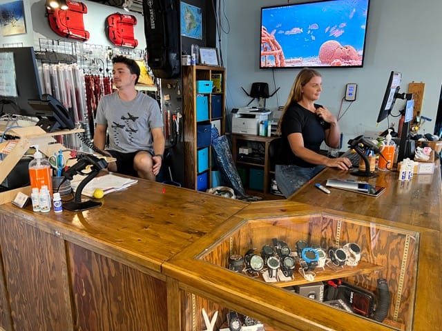 two people sitting at a counter inside a dive shop