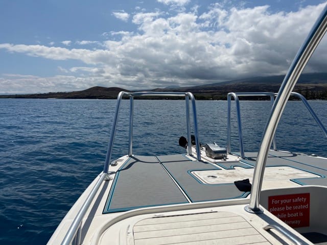 looking out over bow of boat at the ocean surface and Hawaii island in background with clouds overhead