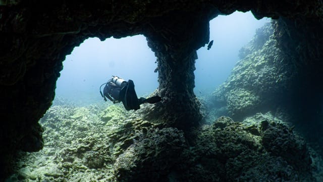 diver swims under a double lava arch