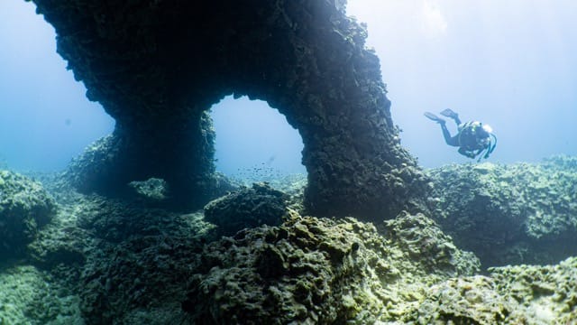 diver swimming under lava rock reef arches