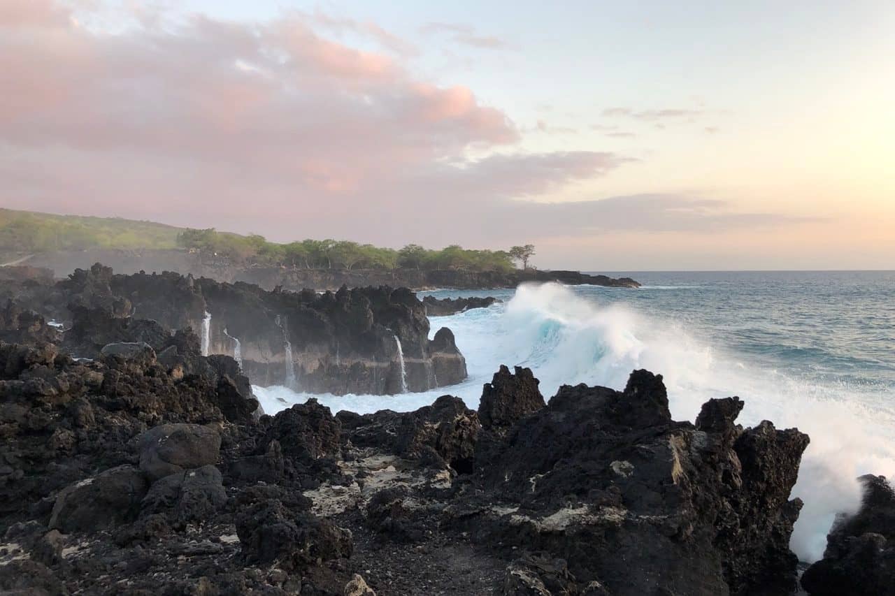 rugged lava rock coast at sunset pounded by ocean waves