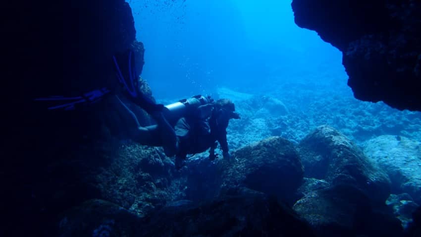 scuba diver swimming under cavern rock