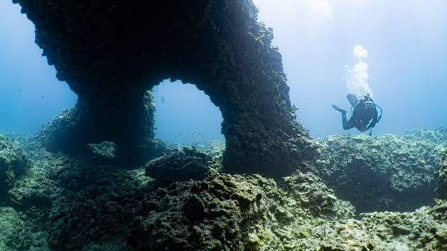 diver swimming under lava rock reef arches