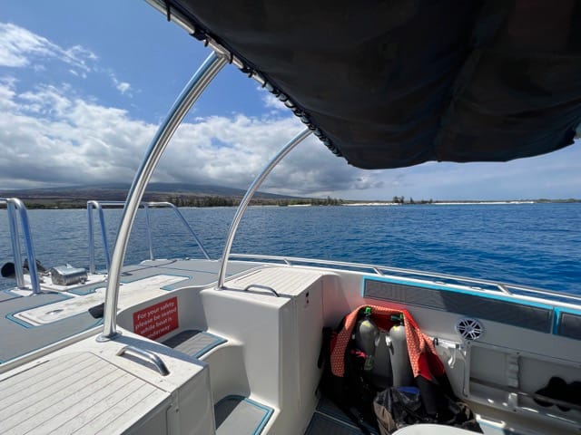 looking out over bow of boat at the ocean surface and Hawaii island in background with clouds overhead