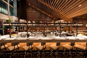 Boqueira’s bar on West 40th street featuring a large white marble countertop and airy vaulted ceilings with rich wood features.