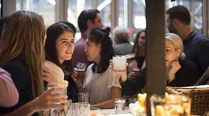 Women smiles among crowd with cocktail in hand while sitting at the bar of Spainish restaurant, Boqueria.
