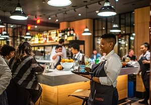 A waiter carrying three drinks to guests at Boqueria Penn Quarter.