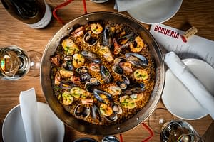 Spanish paella with saffron rice, shrimp, clams and mussels served in a shallow pan served with white wine from Boqueria Spanish restaurant and tapas bar in NYC and DC.