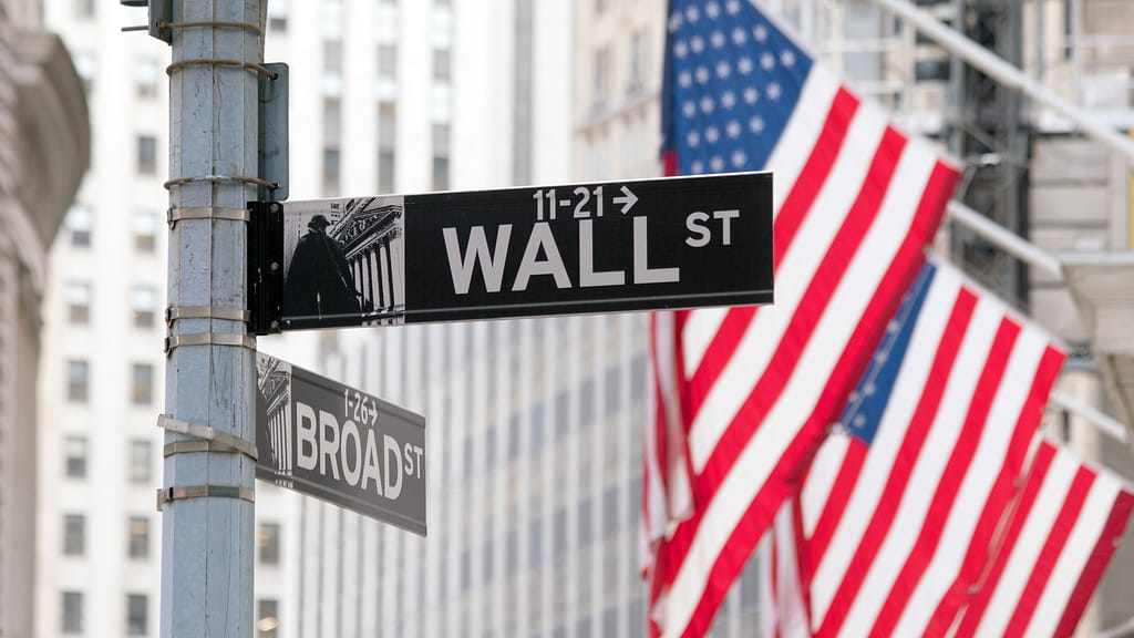 Intersection of Wall St and Broad St signs with American flags and buildings in the background