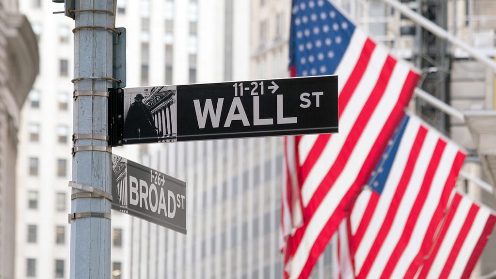 Intersection of Wall St and Broad St signs with American flags and buildings in the background