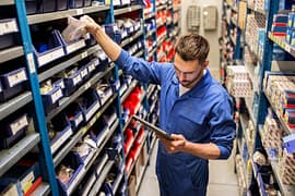 Man looking at a tablet and grabbing parts in a parts warehouse