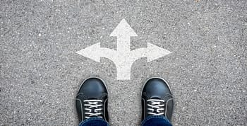 A person's sneakers standing in front of three arrows painted on a road