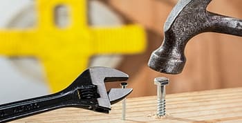 A wrench alongside a nail and a hammer pounding on a screw