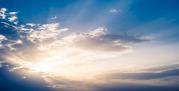 Dispursed white clouds against a blue sky with sunbeams shining through