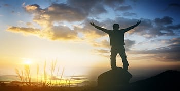 Man standing on a rock with his arms outstretched as the sun comes up over the horizon