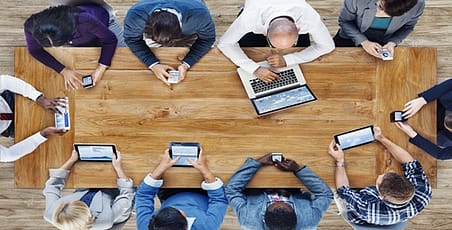 Ariel view of people sitting around a table looking at laptops, tablets and phones