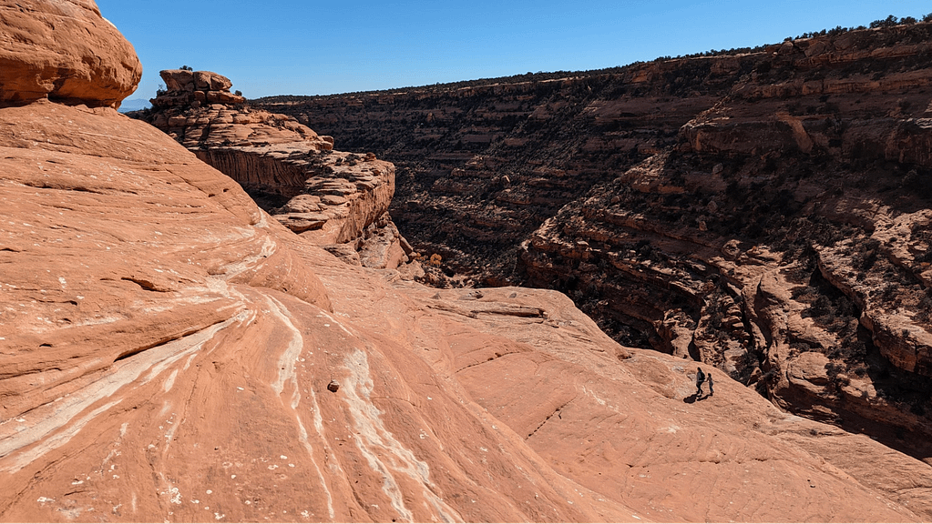 Ribbons of light rock in red rock with hikers in the distance.