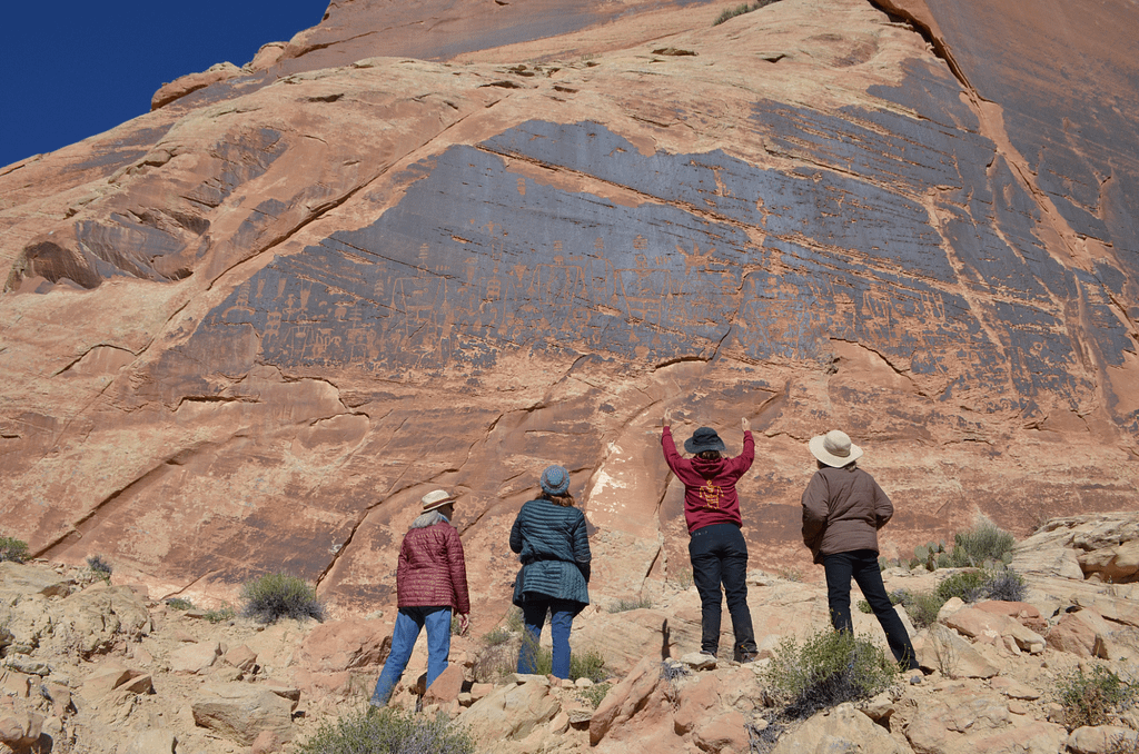 Four women in front of a rock wall in which petroglyphs are carved.