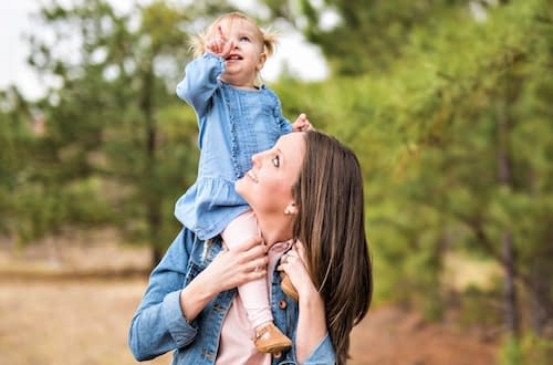 Woman with small child on her shoulders walking through a green space at Azalea Orthopedics.