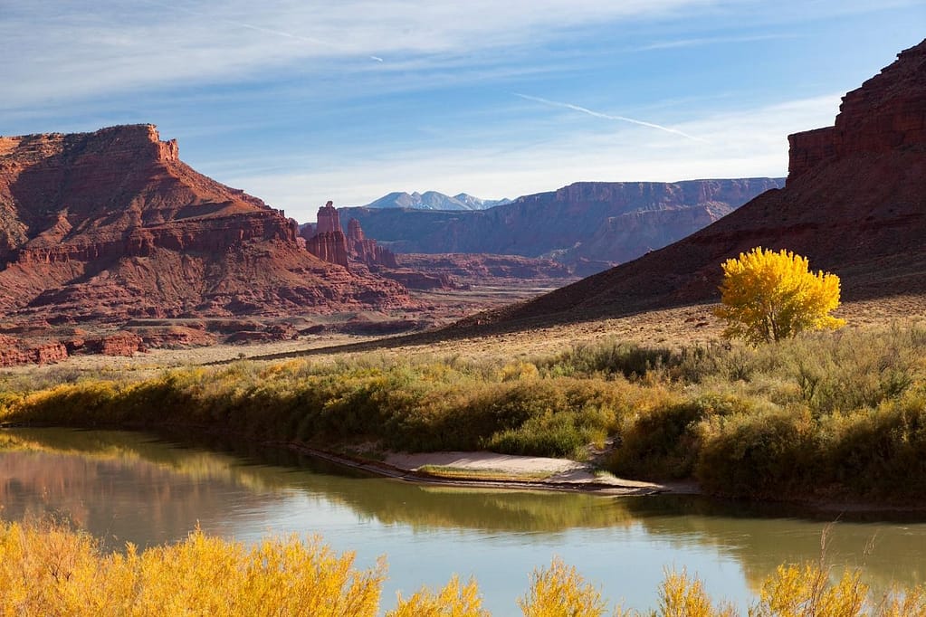 River with reflection of green shore with red rock landscape.