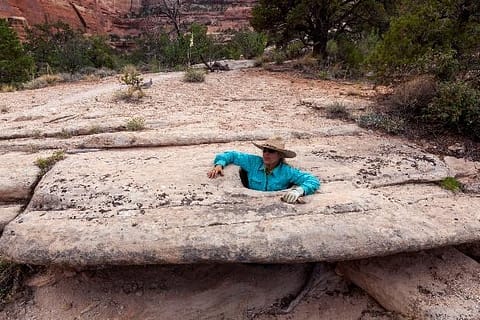 Person standing in a hole in the rock with just their torso and head visible.
