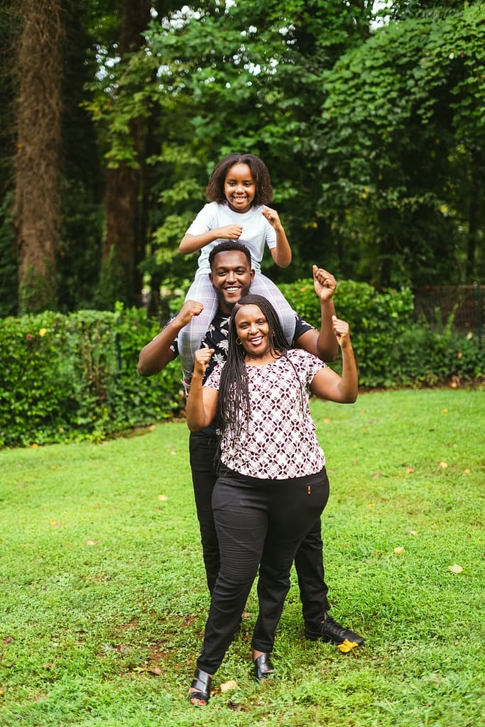 A father holds his daughter on his shoulders while the mom stands in front.
