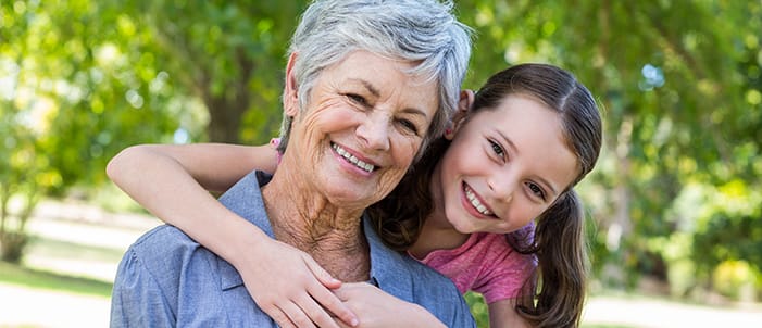Smiling grandmother and granddaughter embracing outdoors, representing multi-generational family dental care and warm, patient-focused oral health services.