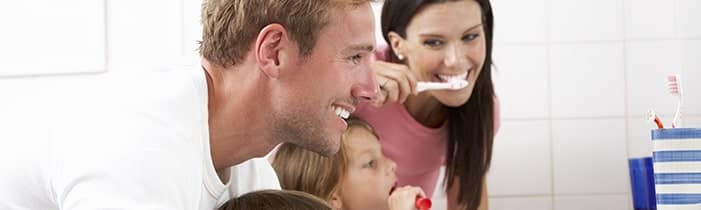 Family brushing teeth together in bathroom, promoting daily oral hygiene routines and preventive dental care for healthy smiles at every age.